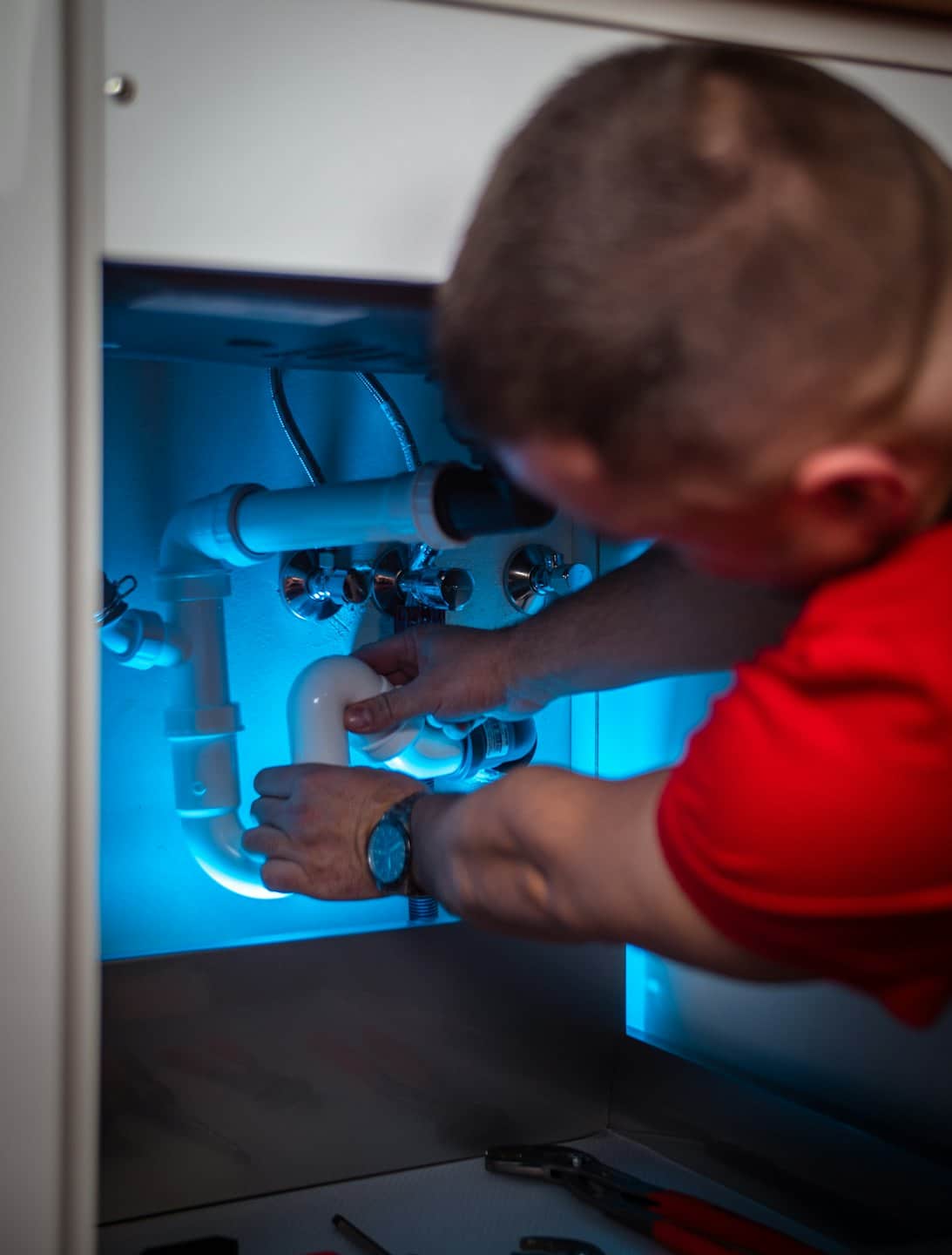 Técnico trabajando en tuberías de PVC bajo un lavabo.