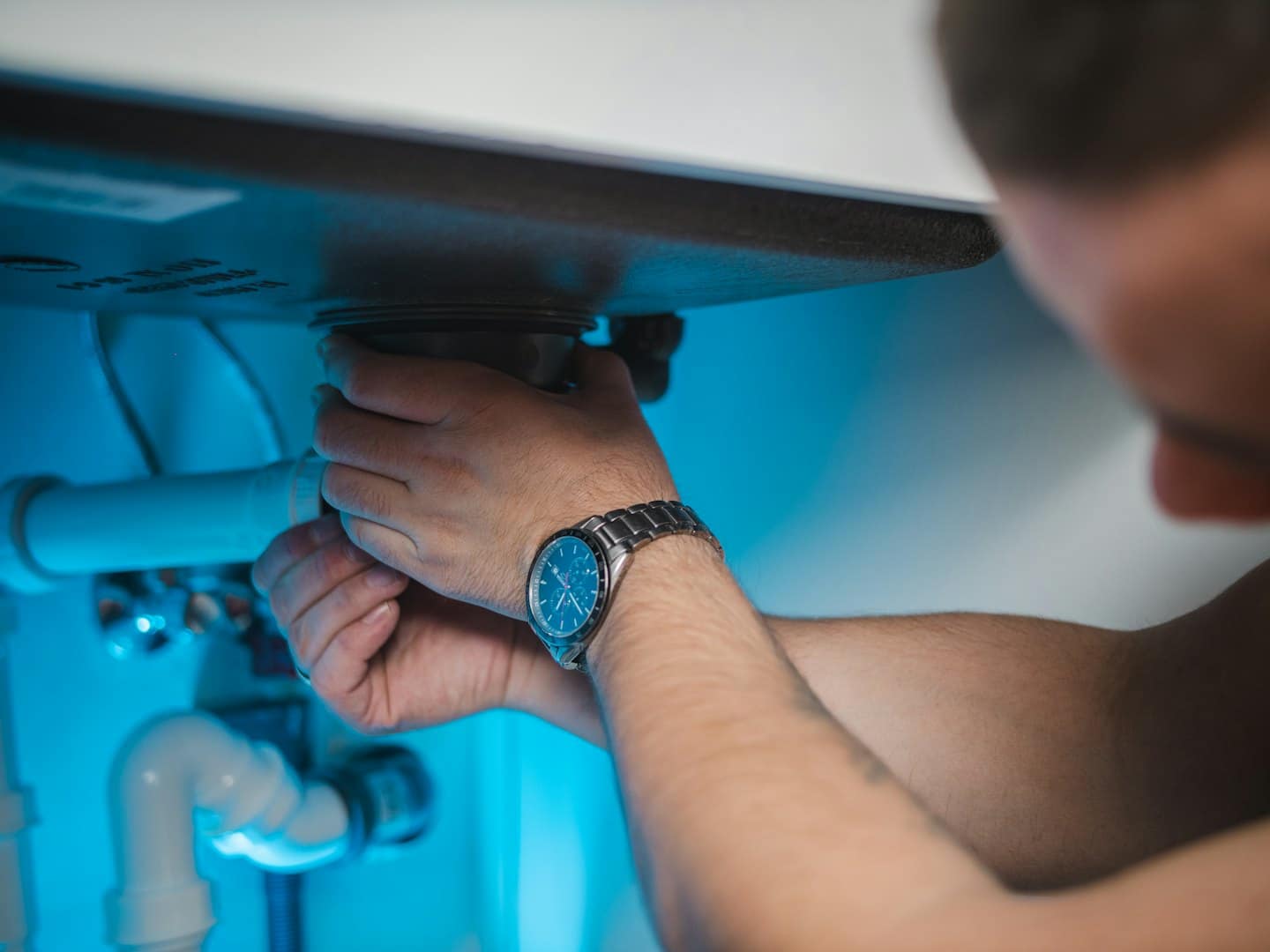 Manos instalando tuberías de PVC blancas bajo un lavabo.